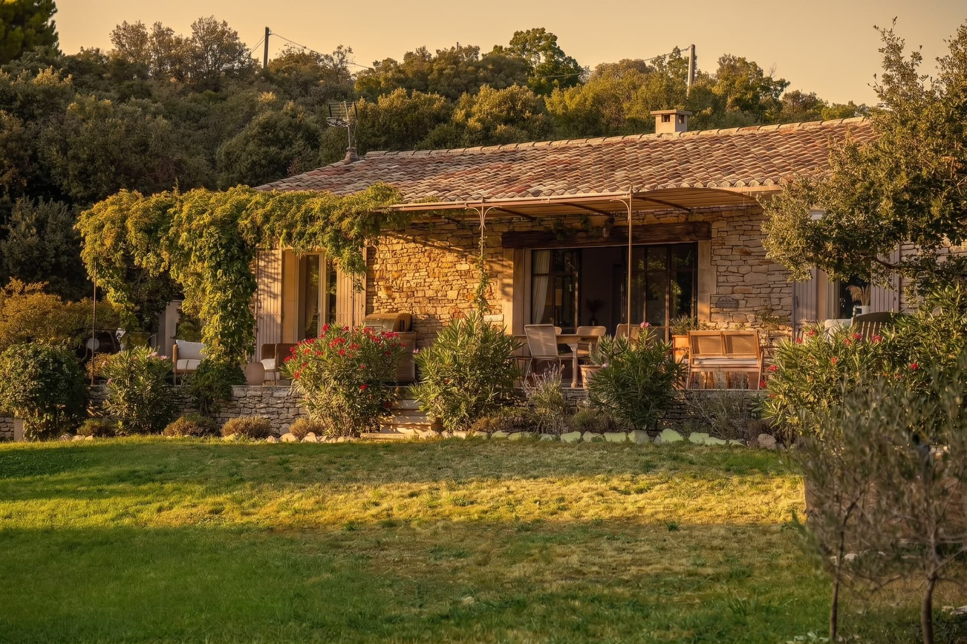 Façade en pierre de la Bastide de la Chênaie, terrasse ombragée au coucher du soleil